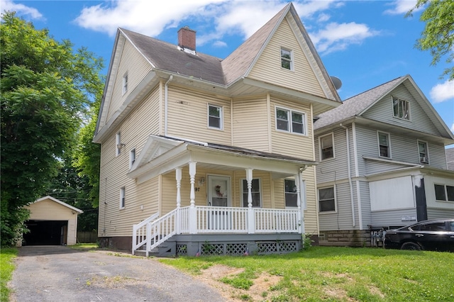 view of front of house featuring an outbuilding, a front lawn, covered porch, and a garage