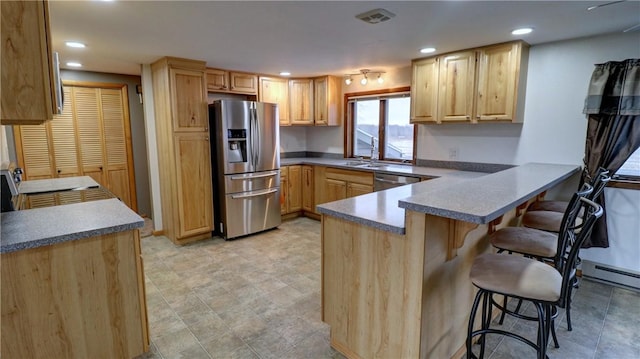 kitchen with kitchen peninsula, appliances with stainless steel finishes, light brown cabinets, and a kitchen breakfast bar