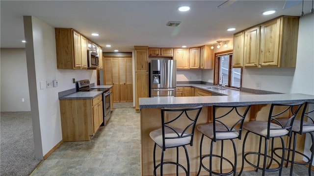 kitchen featuring a kitchen breakfast bar, sink, light colored carpet, kitchen peninsula, and stainless steel appliances