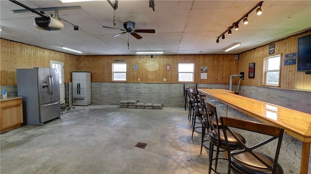 interior space with stainless steel fridge, white fridge, ceiling fan, and wood walls