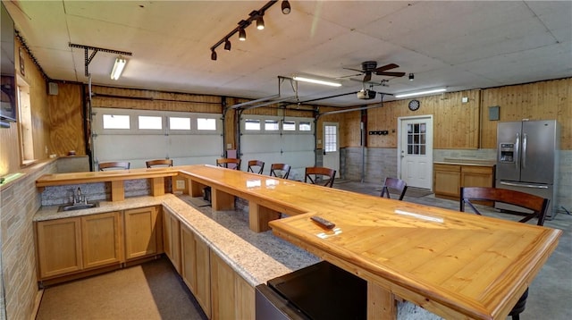 garage with ceiling fan, sink, stainless steel refrigerator with ice dispenser, wood walls, and a garage door opener