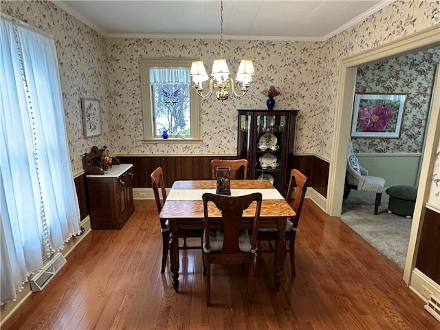 dining room featuring hardwood / wood-style floors, wood walls, ornamental molding, and an inviting chandelier