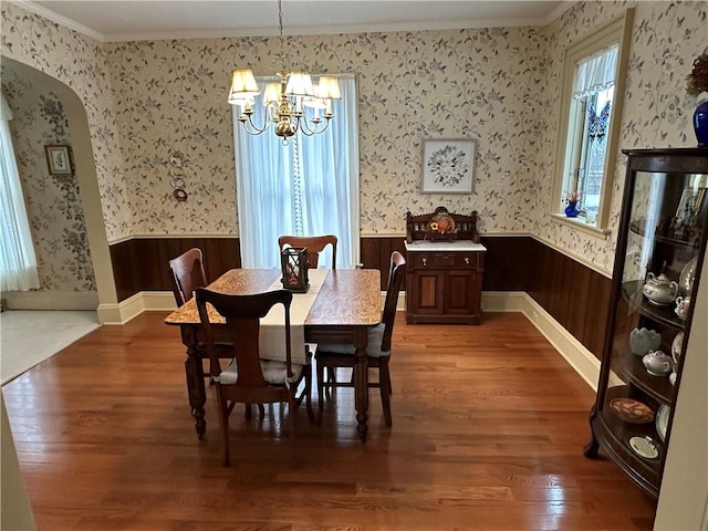 dining room with wood walls, wood-type flooring, crown molding, and an inviting chandelier