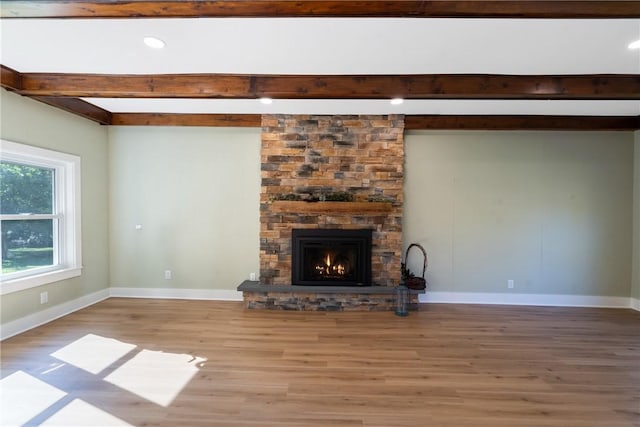 unfurnished living room featuring beam ceiling, light wood-type flooring, and a stone fireplace