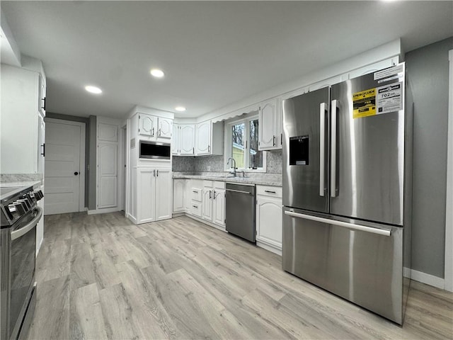 kitchen with appliances with stainless steel finishes, light wood-type flooring, backsplash, sink, and white cabinets