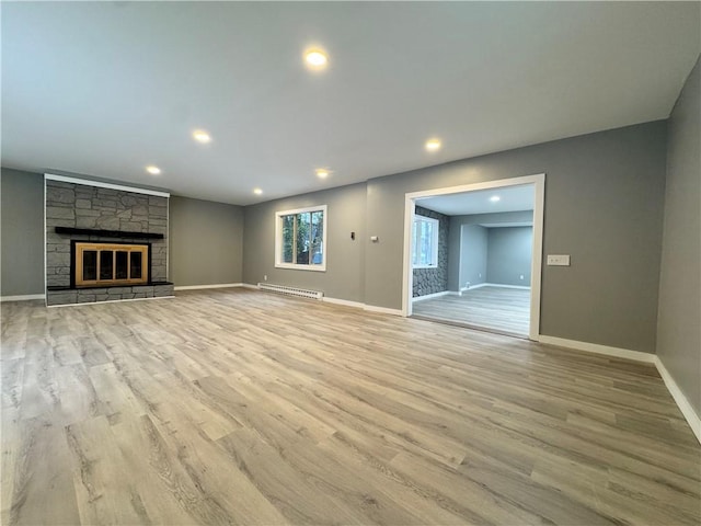 unfurnished living room with a baseboard heating unit, a stone fireplace, and light hardwood / wood-style flooring