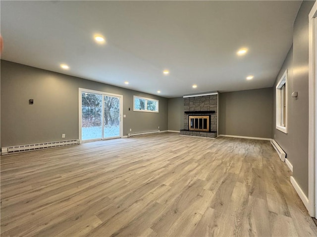 unfurnished living room with a stone fireplace, light hardwood / wood-style flooring, and a baseboard heating unit