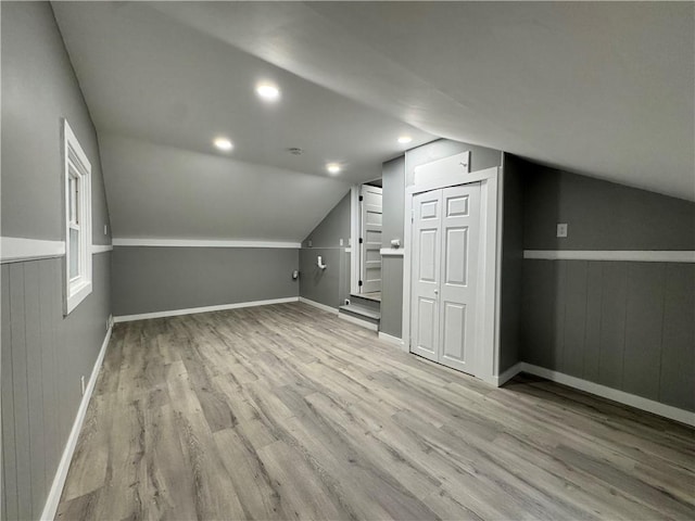 additional living space with light wood-type flooring, vaulted ceiling, and wooden walls