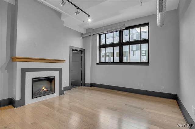 unfurnished living room with light wood-type flooring, a fireplace, and track lighting