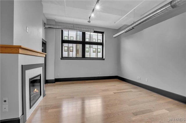 unfurnished living room featuring rail lighting and light hardwood / wood-style flooring