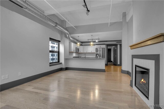 unfurnished living room featuring a tile fireplace, light hardwood / wood-style flooring, and a towering ceiling