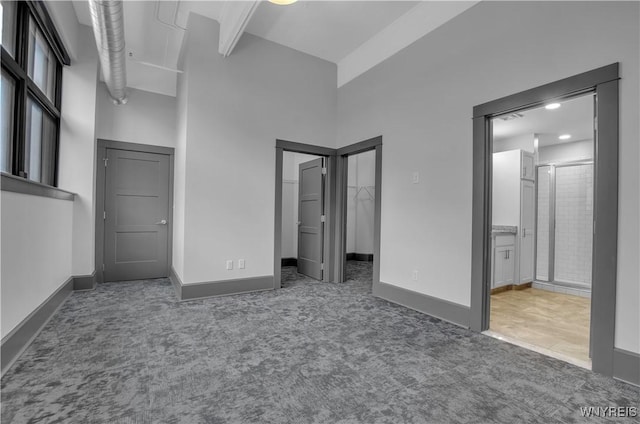 unfurnished bedroom featuring dark carpet, a towering ceiling, and ensuite bath