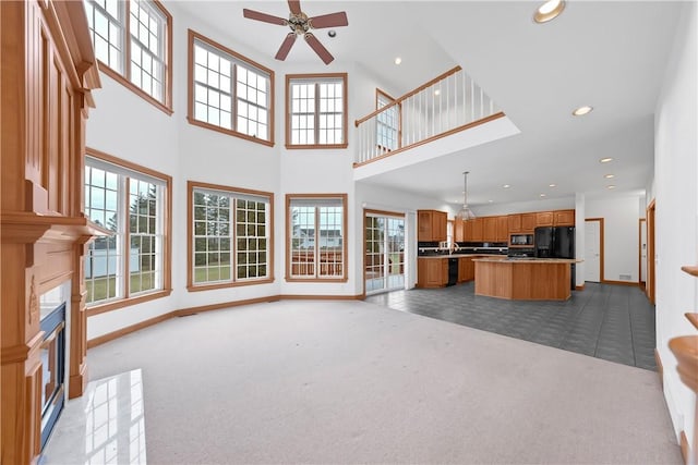 unfurnished living room featuring ceiling fan, light colored carpet, and a high ceiling