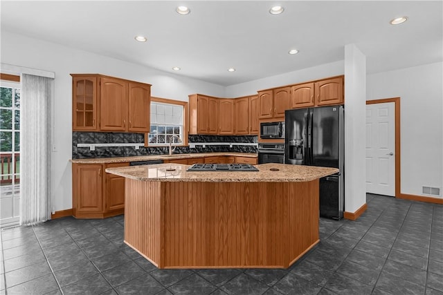 kitchen with black appliances, decorative backsplash, a center island, and light stone countertops