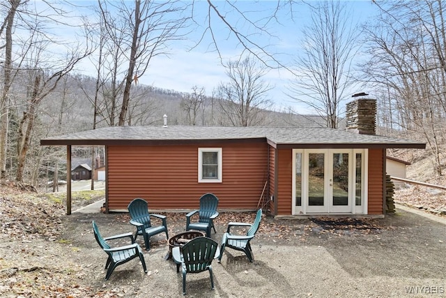 back of house with french doors, a fire pit, a chimney, and a shingled roof