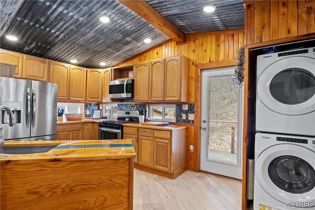 kitchen featuring lofted ceiling with beams, stainless steel appliances, wood walls, stacked washer / dryer, and light wood-type flooring