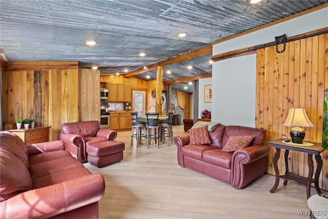 living room featuring a barn door, wooden walls, light wood-style flooring, and vaulted ceiling