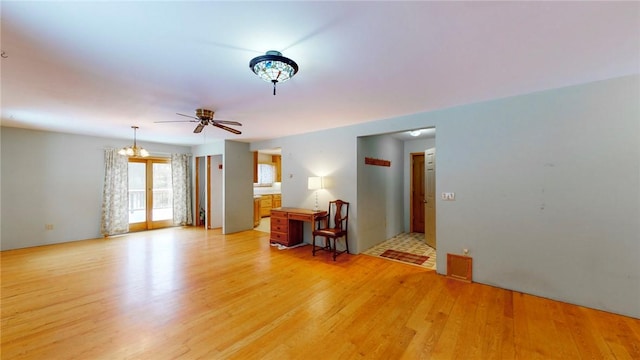 spare room with ceiling fan with notable chandelier and light hardwood / wood-style floors