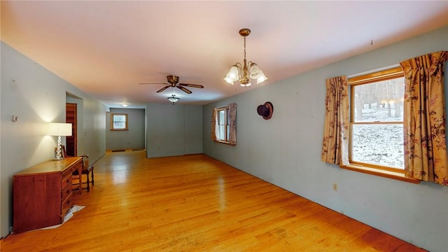 empty room with ceiling fan with notable chandelier and light hardwood / wood-style floors