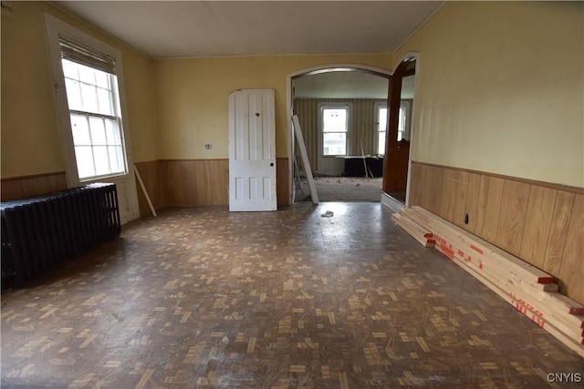 unfurnished room with radiator, a wealth of natural light, and wood walls