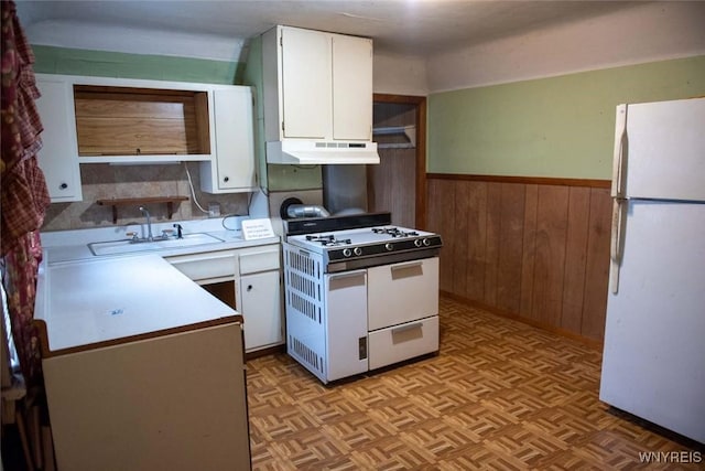 kitchen with white appliances, wooden walls, sink, white cabinets, and light parquet flooring