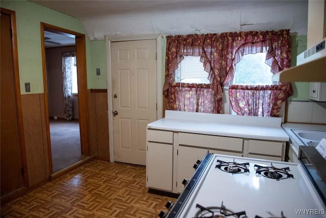 kitchen featuring light parquet flooring, white range, white cabinetry, and wooden walls