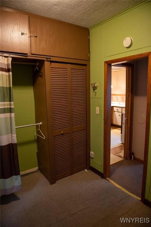 unfurnished bedroom with dark colored carpet, a textured ceiling, and a closet