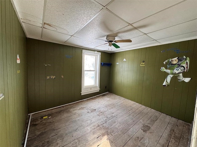 unfurnished room featuring wood-type flooring, a drop ceiling, ceiling fan, and wooden walls