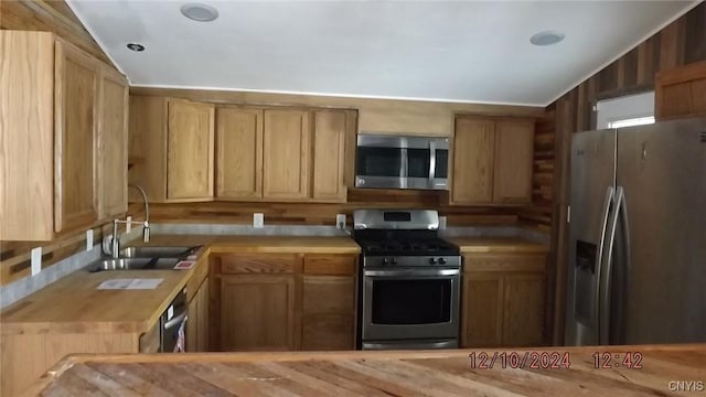 kitchen featuring sink, wood counters, lofted ceiling, wooden walls, and appliances with stainless steel finishes