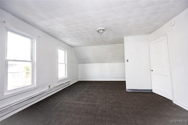 additional living space featuring dark carpet, vaulted ceiling, and a baseboard heating unit