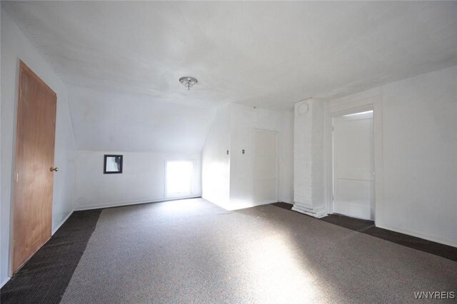 additional living space with dark colored carpet and lofted ceiling