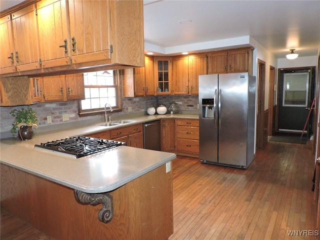 kitchen with kitchen peninsula, light wood-type flooring, backsplash, stainless steel appliances, and sink