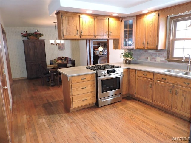 kitchen with pendant lighting, stainless steel gas stove, light hardwood / wood-style floors, and sink