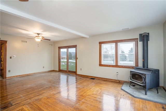 unfurnished living room featuring beam ceiling, light hardwood / wood-style flooring, a wood stove, and ceiling fan