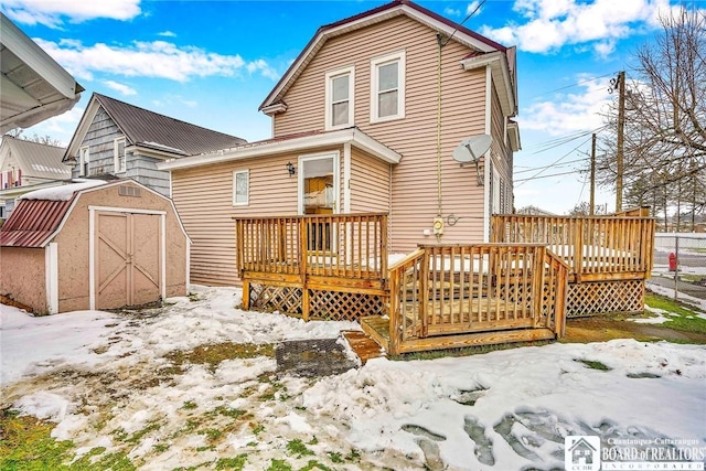 snow covered property with a wooden deck and a storage shed