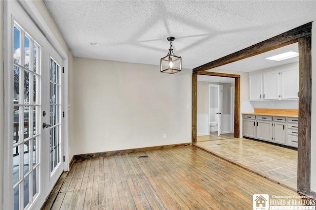 unfurnished dining area featuring french doors, beamed ceiling, light hardwood / wood-style floors, and a textured ceiling