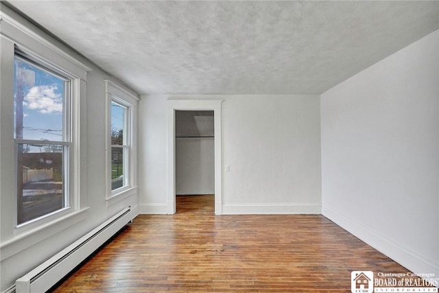 unfurnished bedroom with baseboard heating, a closet, and hardwood / wood-style floors