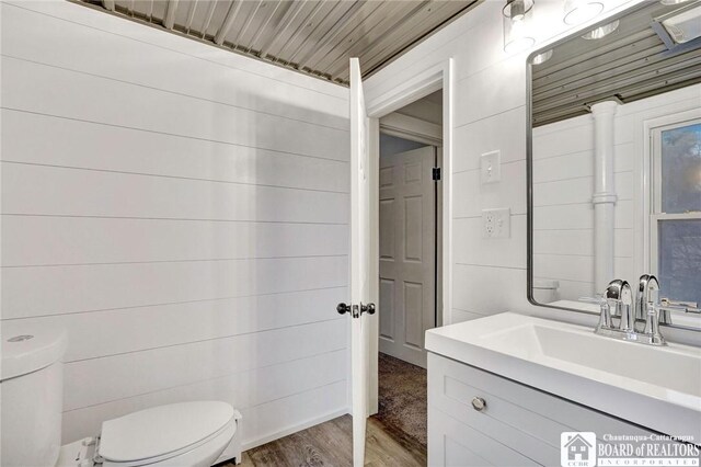 bathroom featuring hardwood / wood-style floors, vanity, wood walls, and toilet