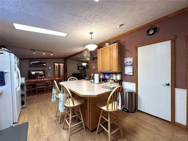 kitchen with a kitchen breakfast bar, a textured ceiling, white refrigerator with ice dispenser, pendant lighting, and light hardwood / wood-style flooring