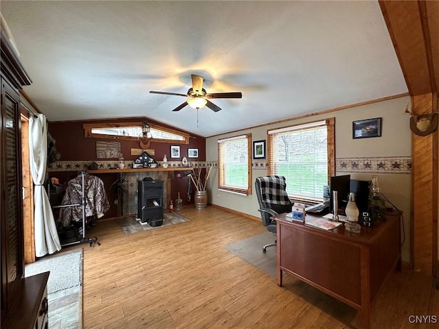 home office featuring light wood-type flooring, vaulted ceiling, ceiling fan, crown molding, and a wood stove