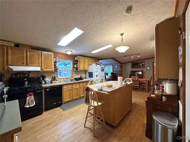 kitchen with a textured ceiling, light hardwood / wood-style floors, hanging light fixtures, and black appliances