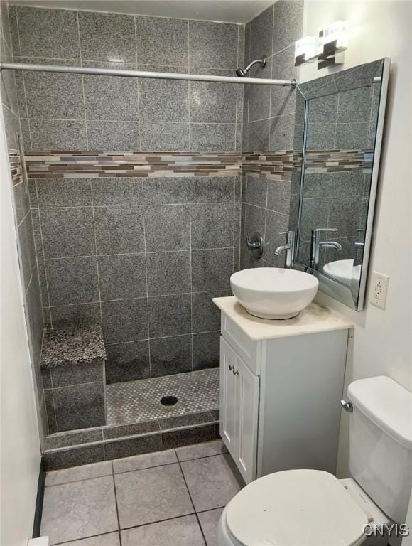 bathroom with toilet, tile patterned flooring, vanity, and tiled shower