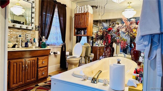 bathroom with a bathing tub, vanity, toilet, and an inviting chandelier