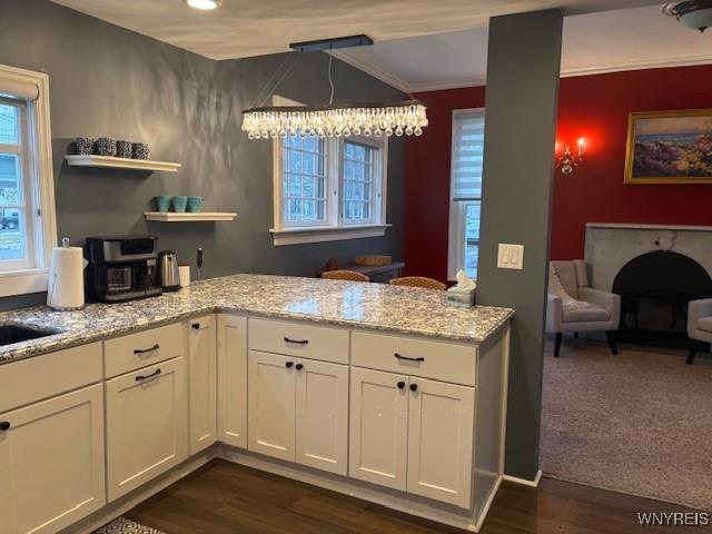 kitchen featuring white cabinetry, light stone counters, dark hardwood / wood-style flooring, kitchen peninsula, and crown molding