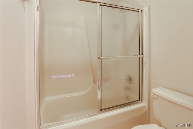 bathroom featuring toilet and shower / bath combination with glass door