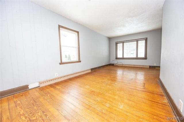 spare room with light hardwood / wood-style floors, baseboard heating, and wood walls