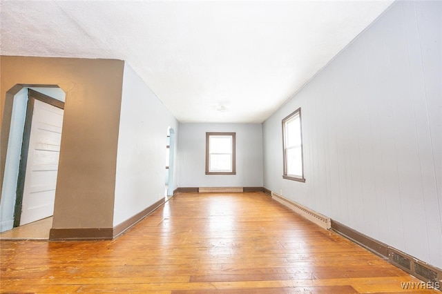 spare room with baseboard heating, wooden walls, and light hardwood / wood-style flooring