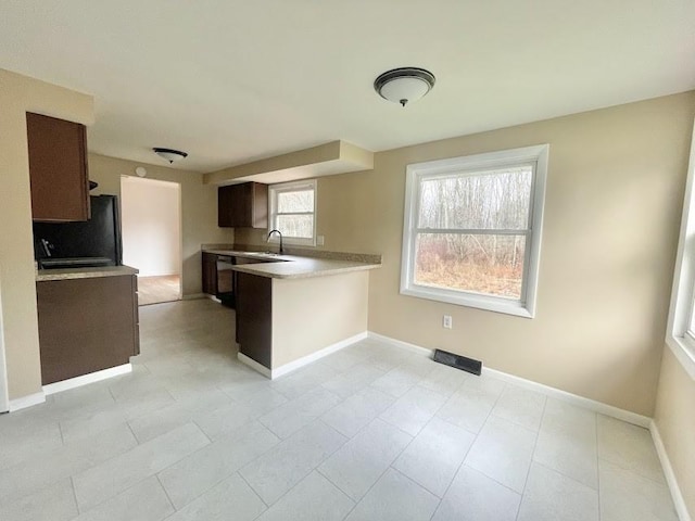 kitchen with black refrigerator, kitchen peninsula, light tile patterned flooring, and sink