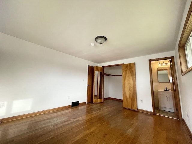 unfurnished bedroom with connected bathroom and dark wood-type flooring