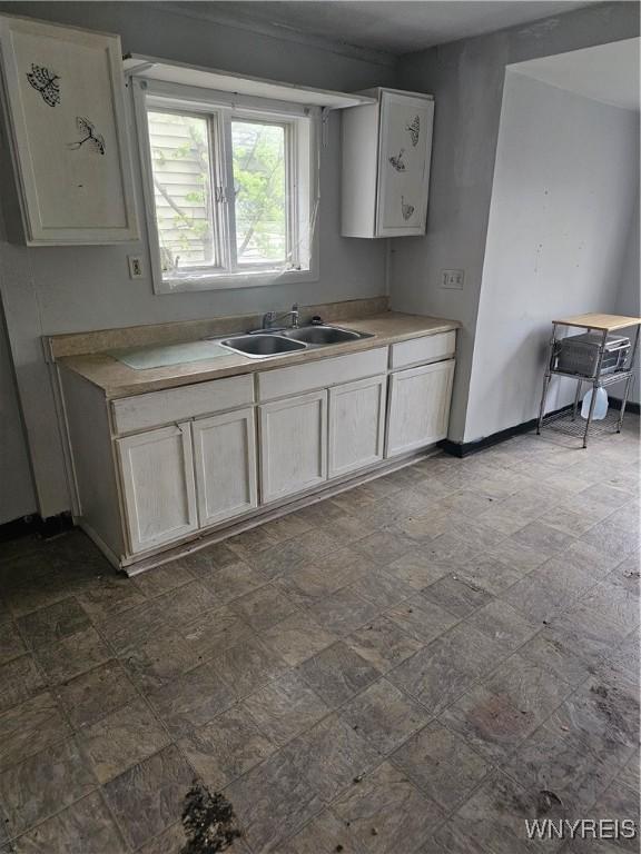 kitchen featuring light countertops, baseboards, stone finish flooring, and a sink